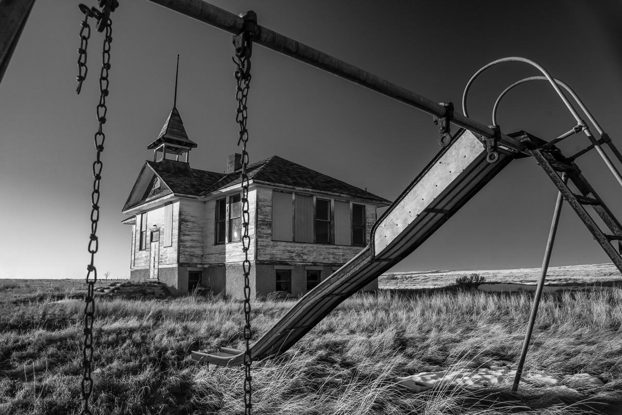 The exterior of the abandoned schoolhouse in Savoy, Montana, framed by a rusted slide.